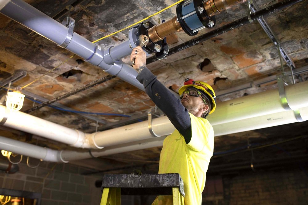 Commercial plumber on ladder installing overhead pipe system